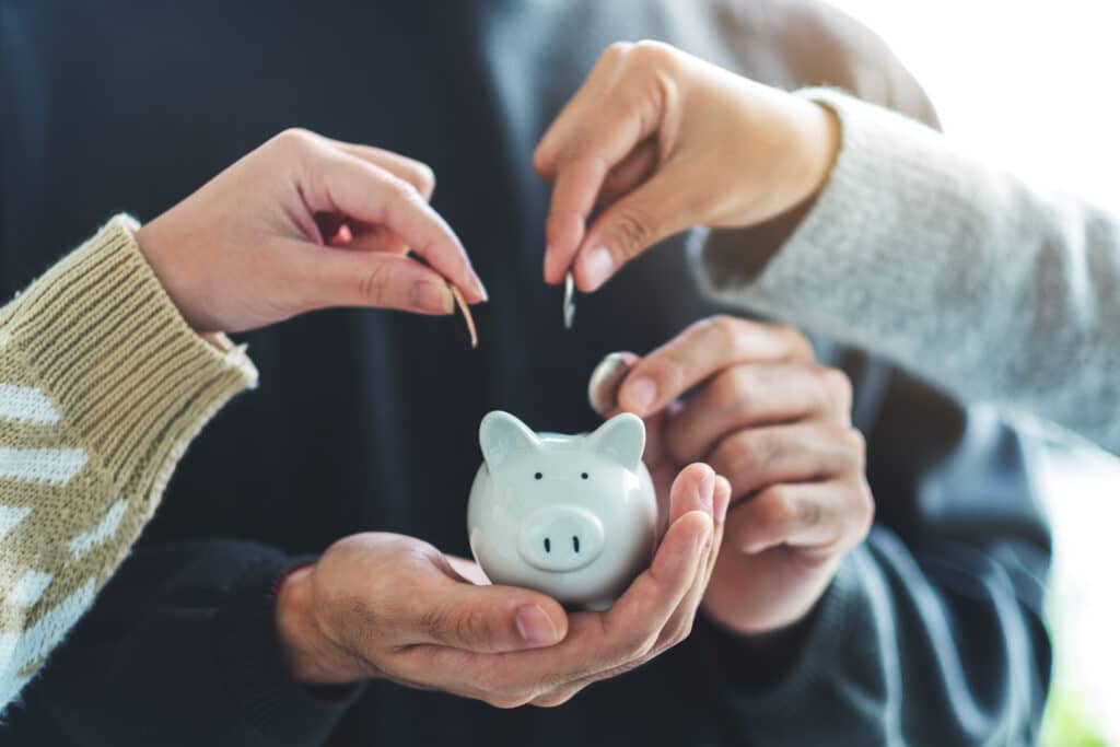 Two people putting money into a piggy bank so the person has secured their programme investment