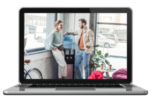 Two people talking together standing around a watercooler shown on the screen of a laptop computer, making in-person connections in the office