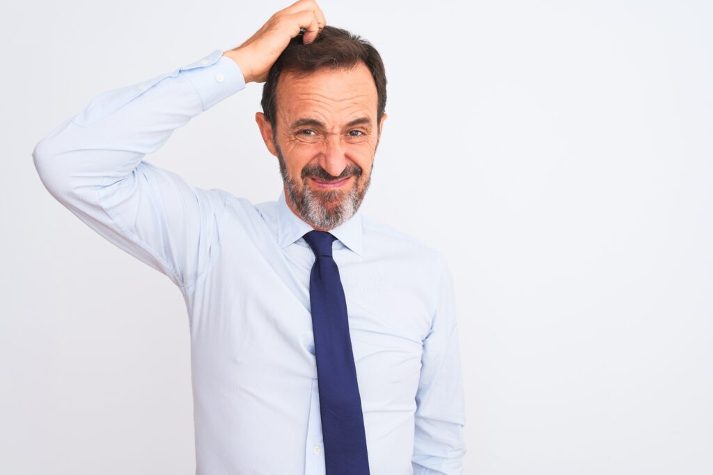 Middle age businessman wearing elegant tie standing over isolated white background confuse and wonder about question. Uncertain with doubt, thinking with hand on head.