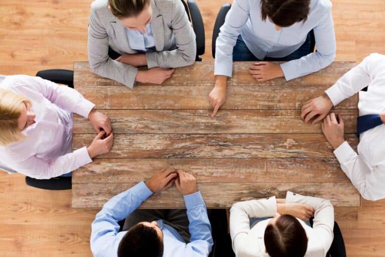 business, people and teamwork concept - close up of creative team sitting at table and pointing finger to something in office