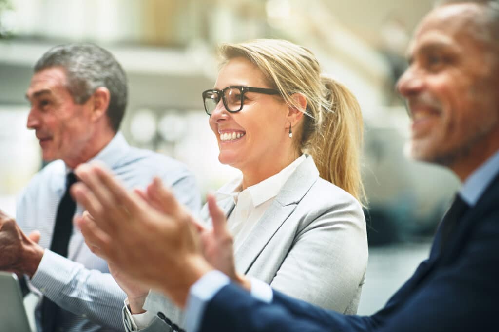 Three businesspeople smiling and clapping during an office meeting