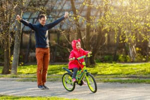 a dad teaching his daughter to ride a bike for the first time, with the daughter balancing on her own confidently