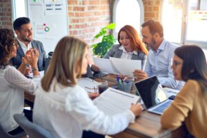 workers around a table discussing new ideas, collaborating and influencing each other to challenge their leadership beliefs 