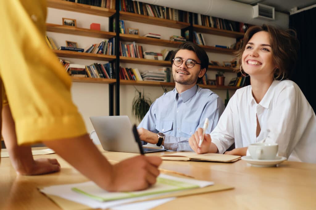 business colleagues sitting at the desk with laptop happily looking at boss who is communicating a new project with them