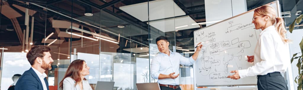 A man conducts a meeting near a flipchart and explains changes the company is going through