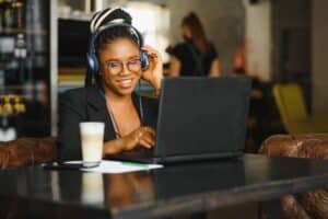 A worker talking to her team online, working from a cafe, sitting with a laptop and a coffee with headphones on, building connections