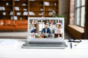 A laptop screen showing multiple smiling faces of 13 people working remotely, joined on to a work call