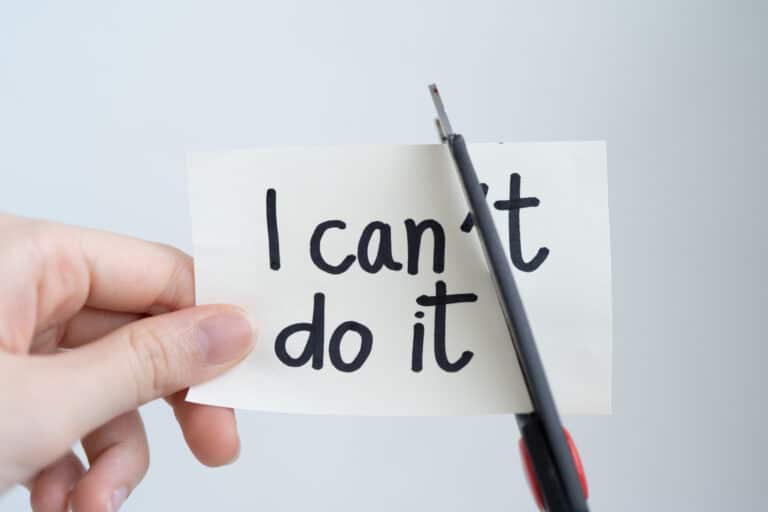 Woman hand cutting paper note with scissors to remove T word "I can't do it" isolated on white background. Positive attitude, self-belief, good self-talk, personal growth, overcome your limiting beliefs, and motivation concept.